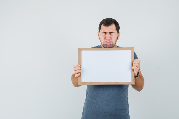 Young male in grey t-shirt holding empty frame and looking upset  