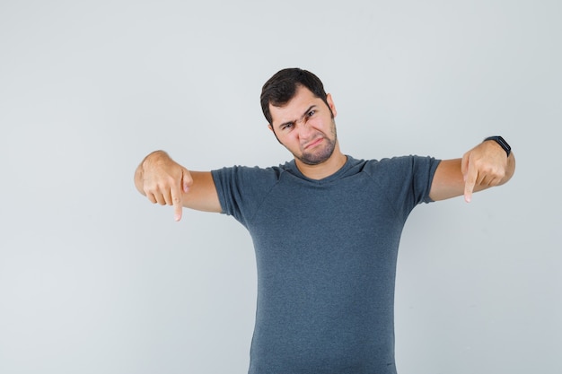 Young male in grey t-shirt pointing down and looking gloomy  