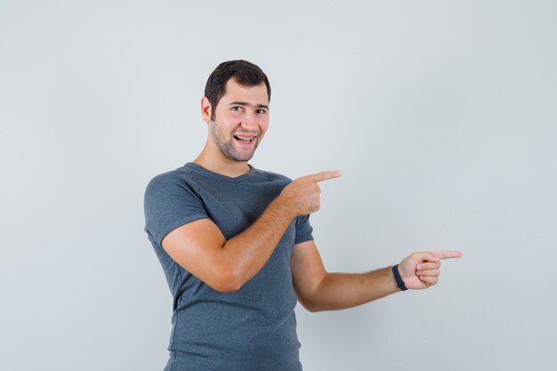 Young male in grey t-shirt pointing to the side and looking cheerful  