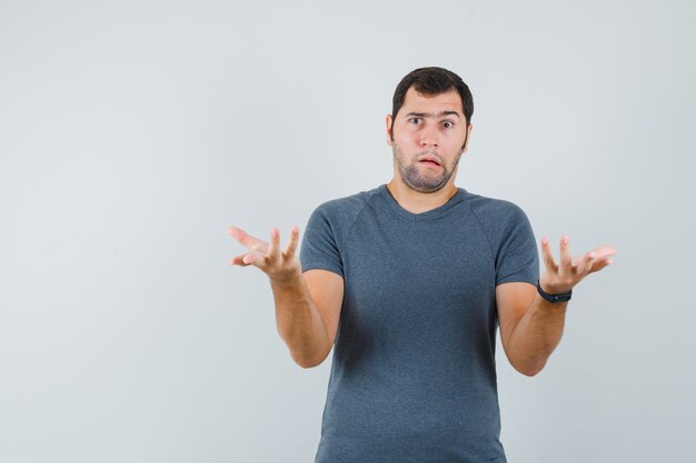 Young male in grey t-shirt showing helpless gesture and looking confused  