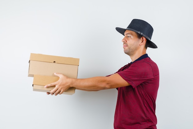 Young male handing boxes in red shirt,black hat and looking calm. .