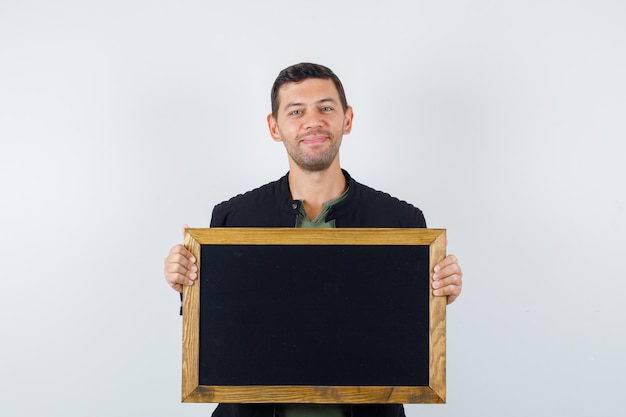 Free photo young male holding blackboard in t-shirt, jacket and looking cheerful. front view.