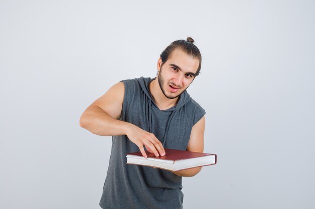 Young male holding book in sleeveless hoodie and looking confident , front view.