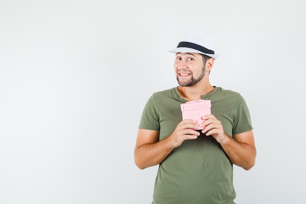 Free photo young male holding gift box in green t-shirt and hat and looking cute