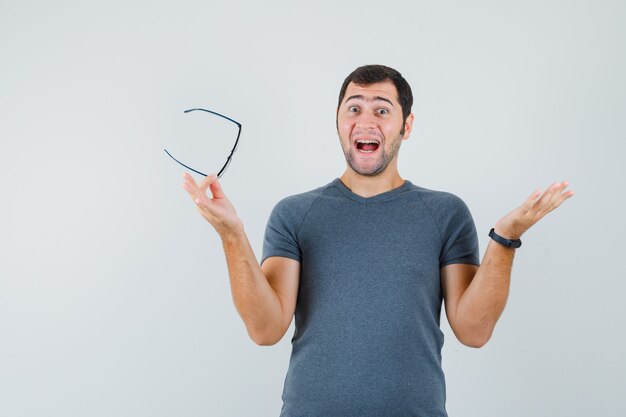 Young male holding glasses in grey t-shirt and looking merry 