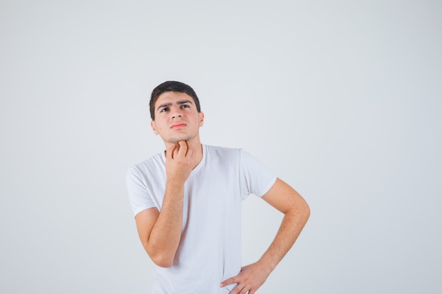 Young male holding hand under chin in t-shirt and looking thoughtful , front view.