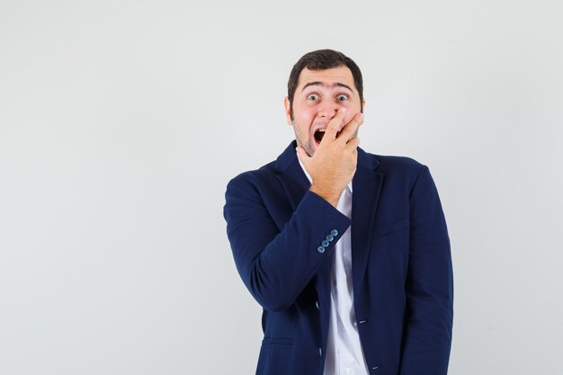 Young male holding hand on mouth in shirt