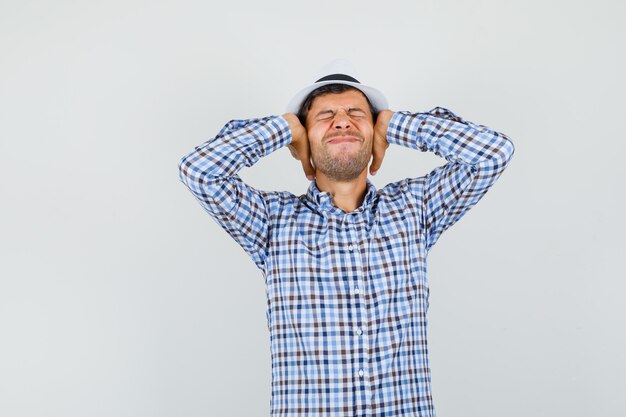 Young male holding hands on ears in checked shirt