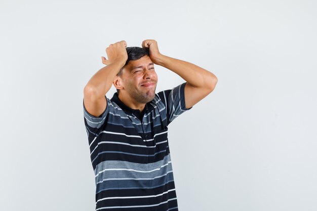 Young male holding hands on head in t-shirt and looking mournful , front view.