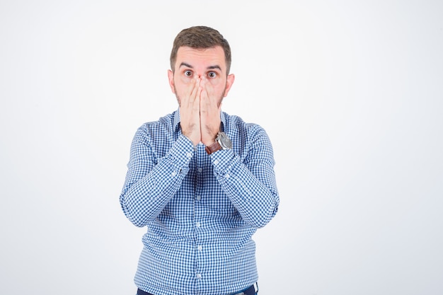 Young male holding hands on mouth in shirt and looking puzzled. front view.