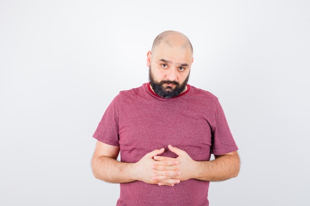 Free Photo young male holding hands together in pink t-shirt and looking sad , front view.