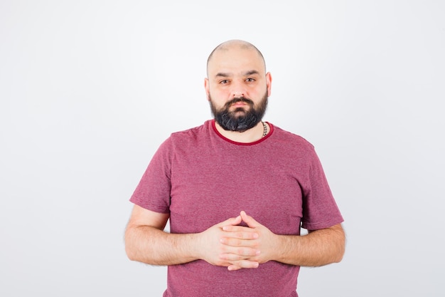 Free Photo young male holding hands together while looking at camera in pink t-shirt and looking calm , front view.