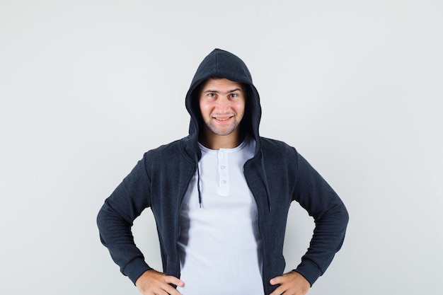 Free photo young male holding hands on waist in t-shirt, jacket and looking confident. front view.