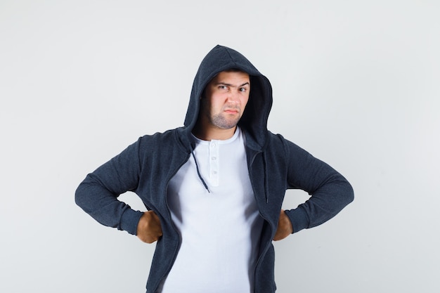 Free photo young male holding hands on waist in t-shirt, jacket and looking spiteful. front view.