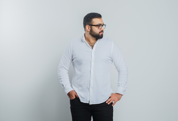 Free photo young male holding hands on waist in white shirt, pants and looking handsome