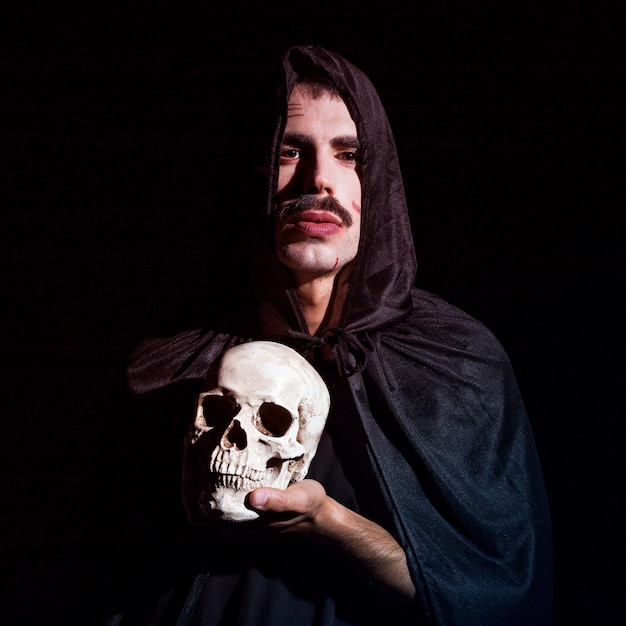 Free Photo young male in hooded cape holding skull