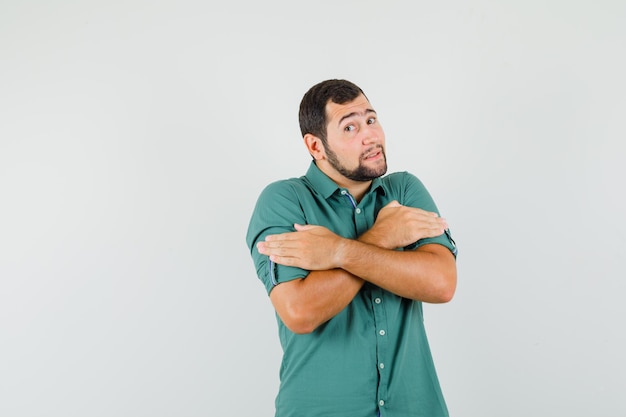 Young male hugging himself while getting cold in green shirt front view.