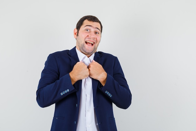 Young male keeping fists on chest in shirt and jacket and looking merry