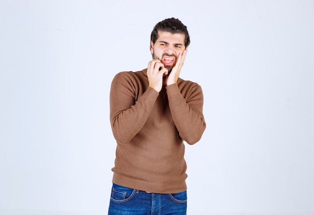 A young male model in brown sweater standing over white wall.