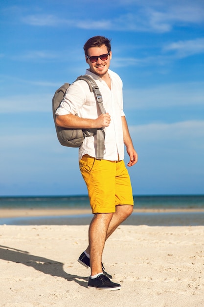 Young male model enjoying summer holiday by the ocean with stylish backpack