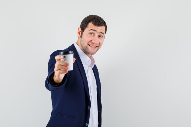 Young male offering cup of coffee in shirt and jacket and looking gentle