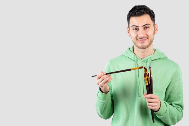 Young male painter holding painting brushes over white