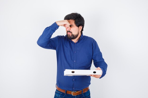 Young male pinching nose due to bad smell in shirt, jeans and looking disgusted. front view.