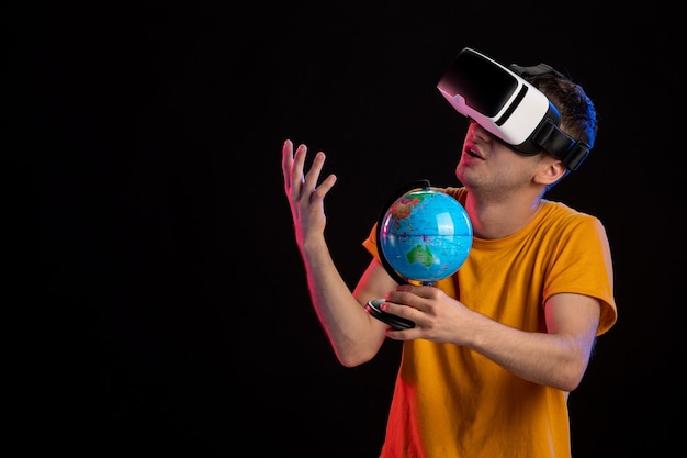 Free photo young male playing virtual reality holding globe on dark surface