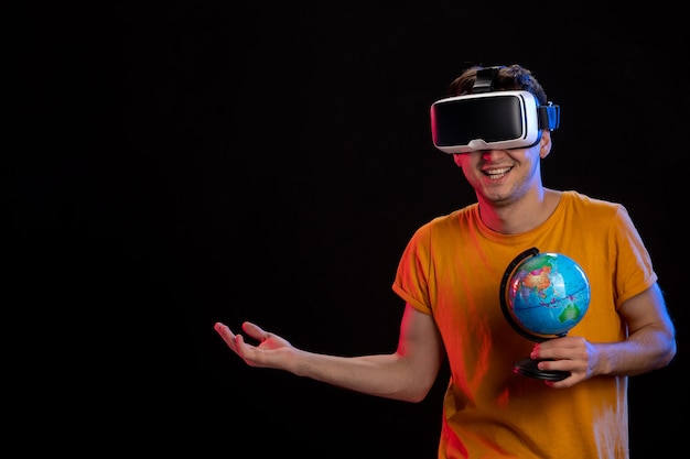 Free photo young male playing virtual reality holding globe on dark surface