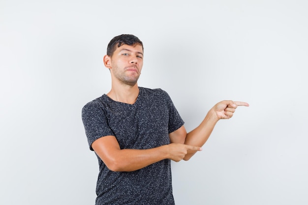 Young male pointing aside in black t-shirt and looking assured , front view.