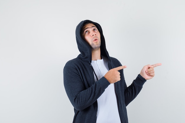 Young male pointing aside in t-shirt, jacket and looking pensive , front view.