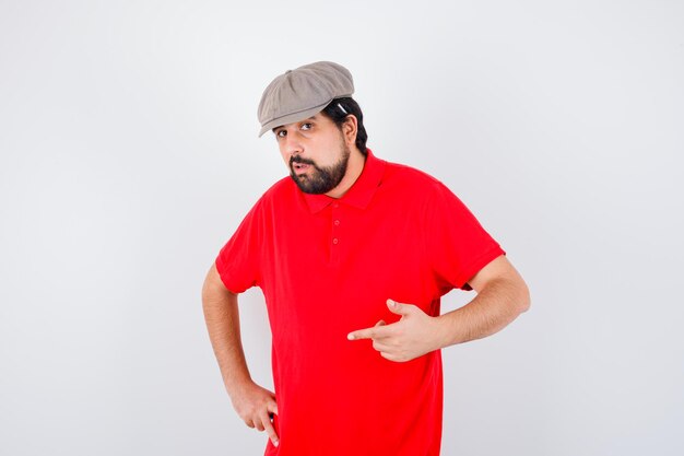 Young male pointing forward in red t-shirt,cap and looking confident. front view.