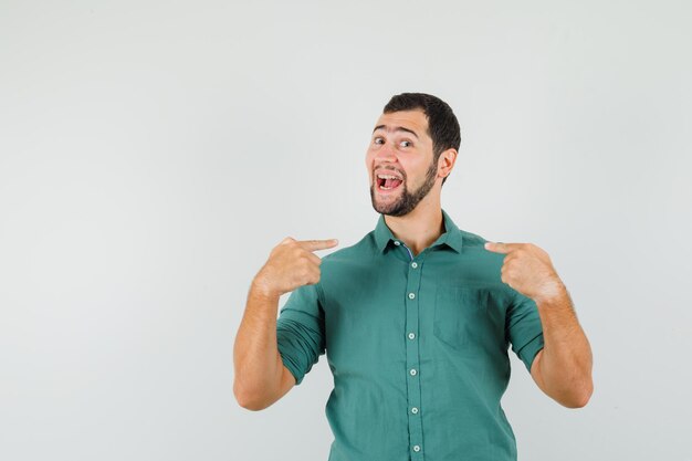 Young male pointing at himself in green shirt and looking cheerful. front view.