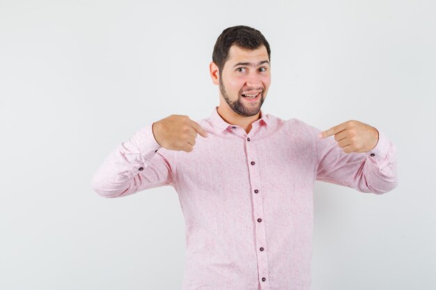 Young male pointing at himself in pink shirt and looking proud 