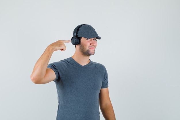 Free photo young male pointing at his headphones in t-shirt, cap and looking cheery. front view.