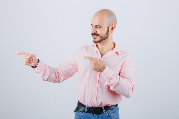 Young male pointing to the left side in shirt, jeans and looking confident , front view.