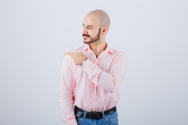 Young male pointing to the left side in shirt, jeans and looking confident. front view.