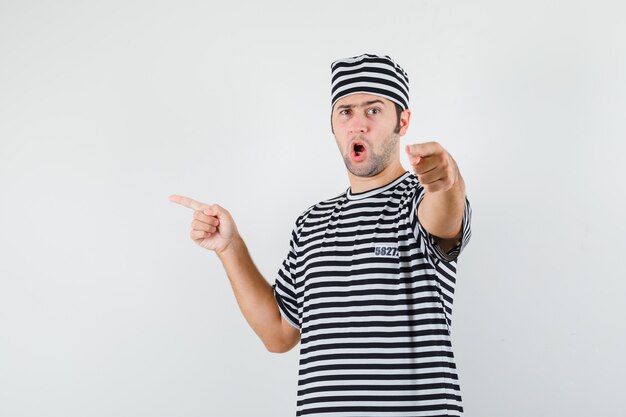 Young male pointing to the left side in t-shirt, hat and looking confident. front view.