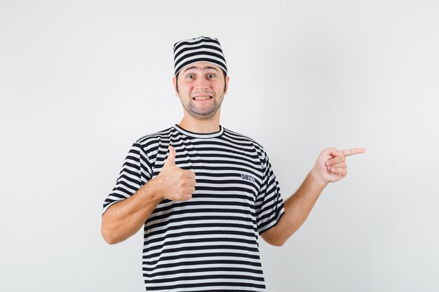 Young male pointing to the right side, showing thumb up in t-shirt, hat front view.