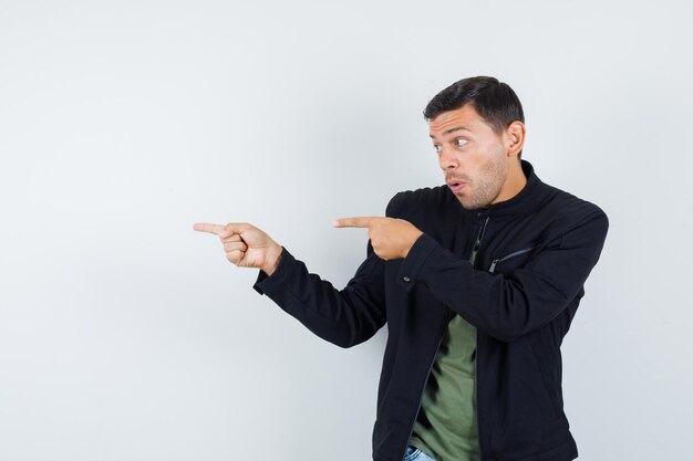 Young male pointing to side in t-shirt, jacket and looking sure. front view.