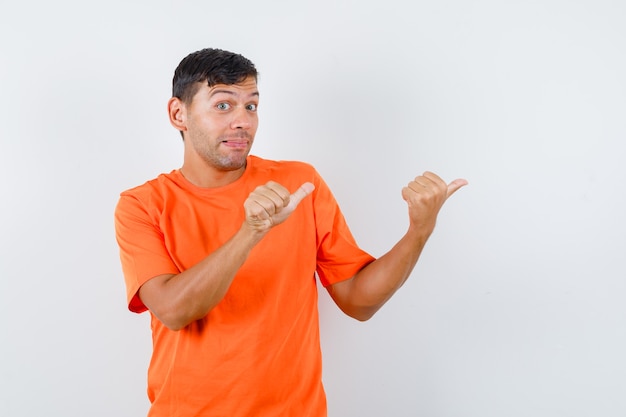 Young male pointing thumbs away in orange t-shirt and looking aware