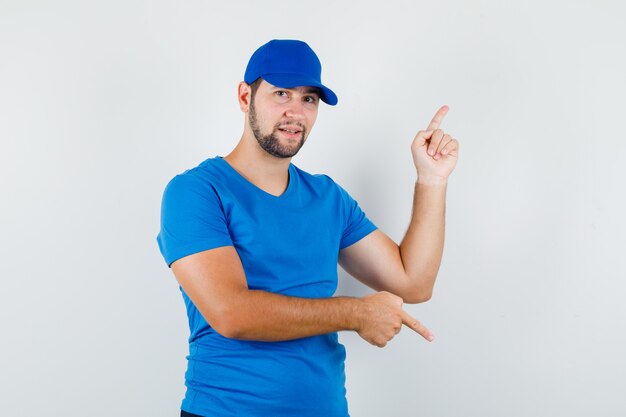 Young male pointing up and down in blue t-shirt and cap and looking positive