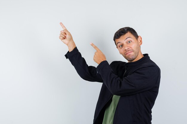 Young male pointing up in t-shirt, jacket and looking cheery. front view.