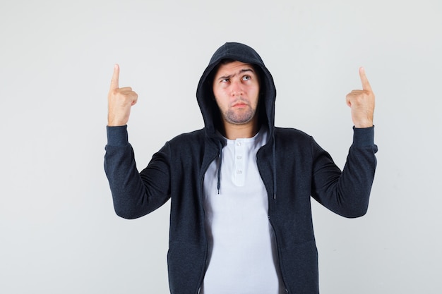 Free Photo young male pointing up in t-shirt, jacket and looking hesitant. front view.