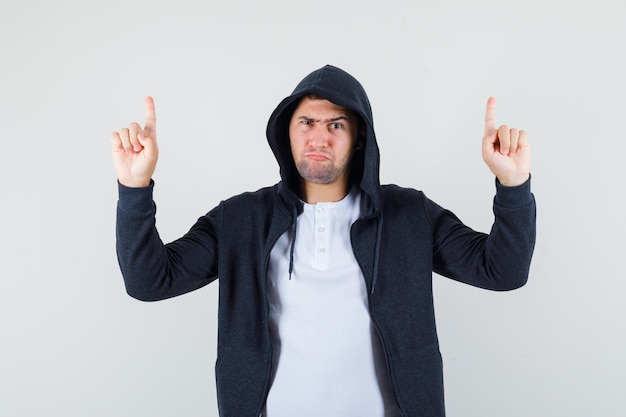 Free Photo young male pointing up in t-shirt, jacket and looking strict. front view.