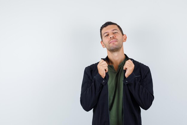 Young male pulling collar of his jacket in t-shirt, jacket and looking cool. front view.