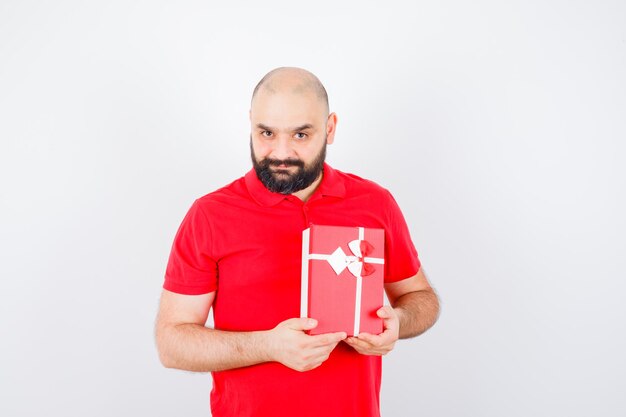 Young male in red shirt showing gift box and looking pleased , front view.