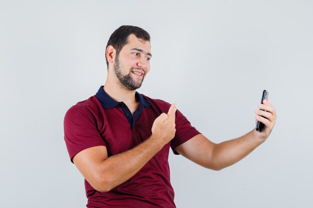 Young male in red t-shirt posing while taking photo and looking jolly , front view.