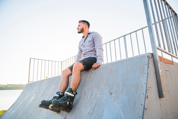 Young male rollerskater sitting in skate park