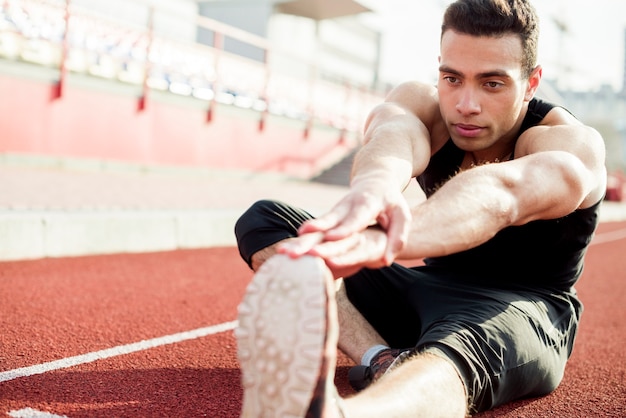 Free photo young male runner stretching her hands while exercising at stadium